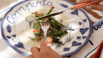 Person cutting vegetables on a decorative plate with blue designs.