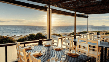 Beachfront restaurant with wooden tables and sunset view over the ocean.