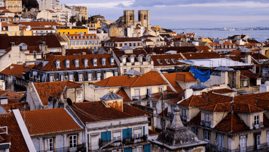 Rooftops of Lisbon with red tiles and distant sea view.