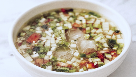Bowl of vegetable soup with diced onions, tomatoes, and peppers.