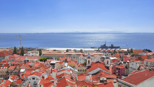 Aerial view of a coastal town with red rooftops and calm blue sea.