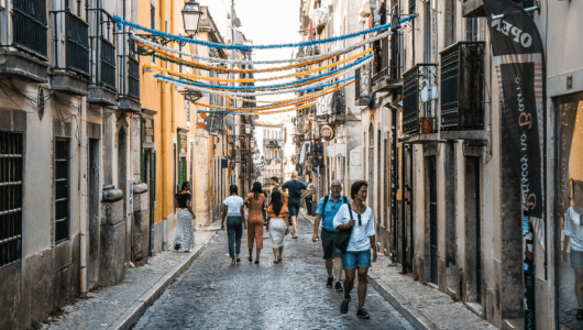 People walking on a narrow cobblestone street with colorful streamers above.