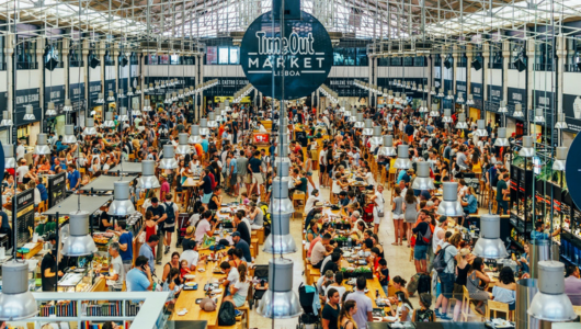Crowded food market with people dining and socializing at tables.