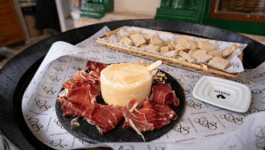 Cheese wheel with cured meat and bread chunks on a tray.