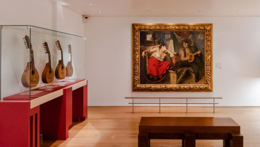Art gallery with mandolins in a display case and a painting on the wall.