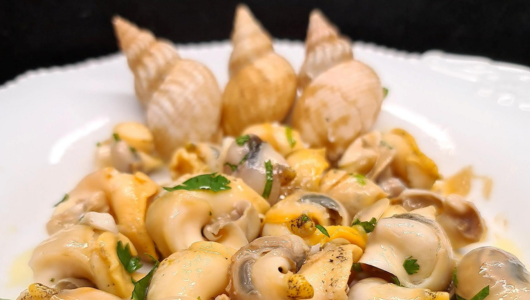 Cooked snails in a dish with herbs, garnished with three conical shells.