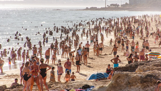 Crowded beach with many people swimming and sunbathing on a sunny day.