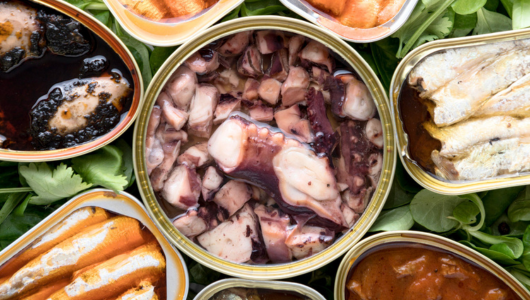 Open cans of assorted seafood placed on leafy greens.