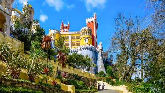 Colorful hilltop castle in Sintra, Portugal, with trees and blue sky in the background.