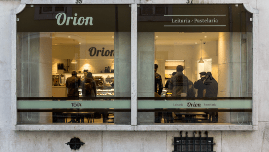 Street view of a bakery with people inside, seen through large windows.
