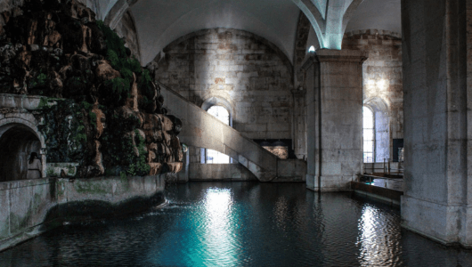 Underground stone hall with reflective pool and moss-covered walls.