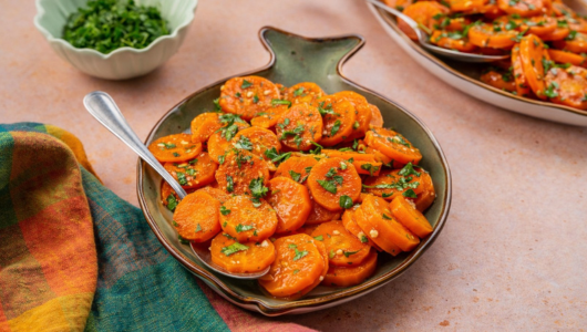 Sliced carrots with herbs in a fish-shaped dish, colorful cloth beside.