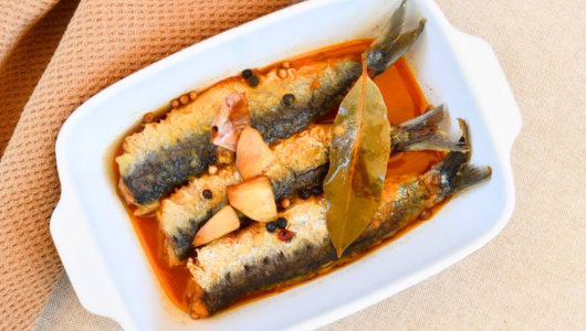 Three cooked fish in sauce with spices in white dish.