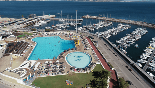Aerial view of a swimming pool and marina with many boats docked.