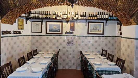 Cozy restaurant with brick arch ceiling, tables set, wine bottles and framed art on walls.