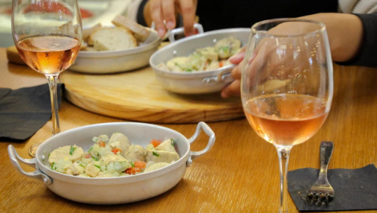 People dining with rose wine and dishes on a wooden table.