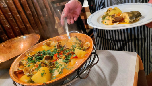 Person serving seafood stew from pot to plate on a table.