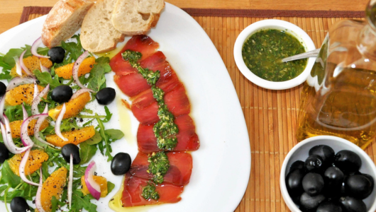 Plate with sliced meat, salad, bread, and olives, plus a sauce bowl and olive oil bottle.