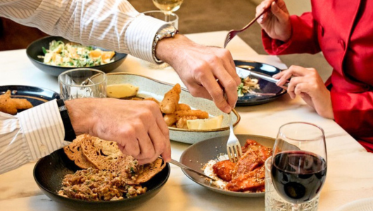 People dining with various dishes on a table, including wine and bread.