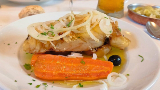 Plate with fish, sliced onions, a carrot, and olives in sauce.