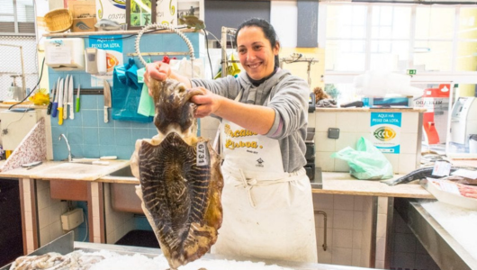Person holding a large fish in a seafood market, smiling.