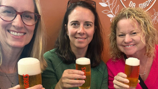 Three women smiling, holding glasses of beer.