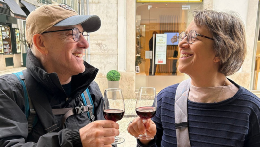 Two people smiling and clinking wine glasses outdoors.