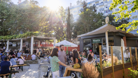 People socializing at an outdoor café with trees and a building in the background.