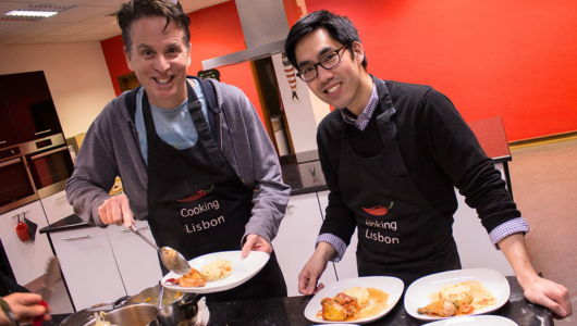 Two people in aprons serving food on plates in a kitchen setting.
