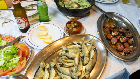 Table with fried fish, salad, sausages, sauces, and drinks.