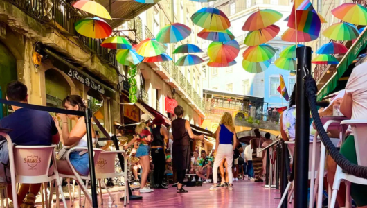 Vibrant street scene with colorful umbrellas overhead and people dining outdoors.