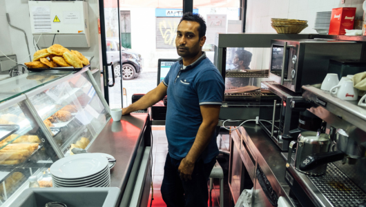 Man standing behind counter in a small bakery or cafe.