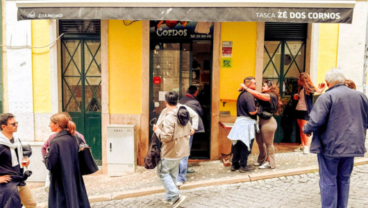 People socializing outside a yellow building with 'Tasca Zé dos Cornos' signage.