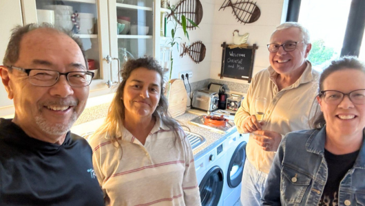 Four adults smiling in a home kitchen with decor and appliances.