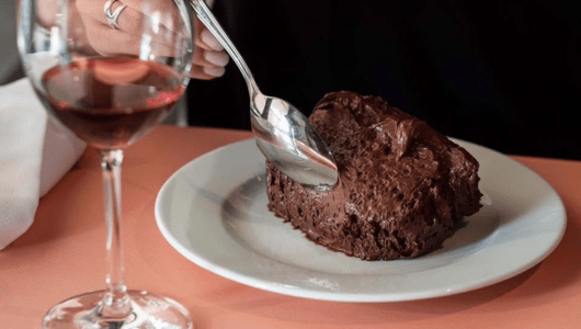 Person scooping chocolate dessert on a plate with a wine glass nearby.