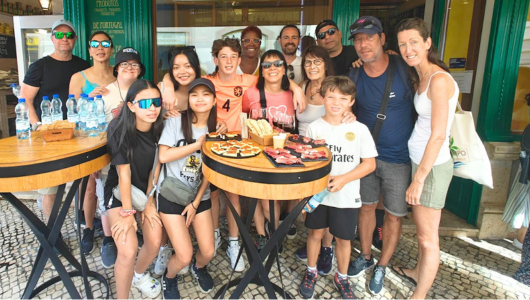 Group of people posing outdoors by tables with snacks and water bottles.