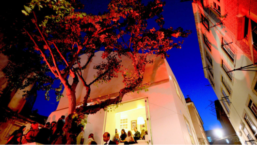 Building with a red-lit tree outside at dusk, people gathered at entrance.