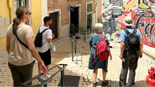 Four people walking down narrow cobblestone street with vibrant mural on wall.