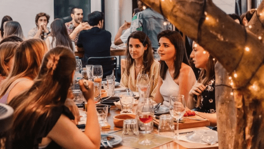 Group of people dining at a restaurant with a tree wrapped in lights nearby.