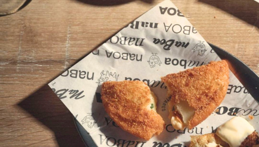 Two breaded snacks on paper in a tray on a wooden table.