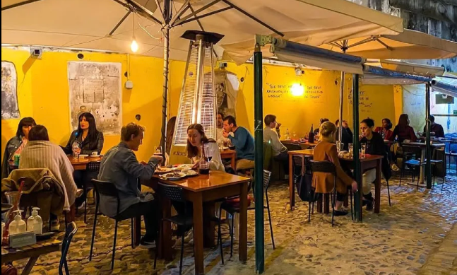 People dining at an outdoor patio with yellow walls and umbrellas.