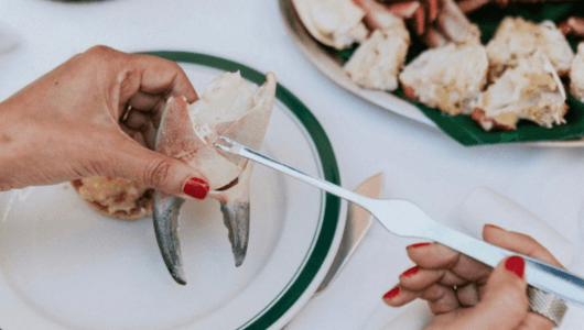 Person eating crab with silver utensils at a dining table.