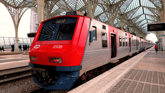 Red and gray passenger train at modern train station with arched roof.