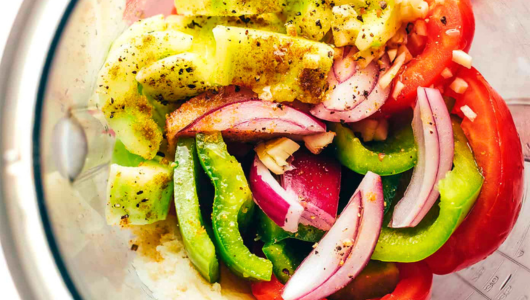 Chopped vegetables in a blender, including tomatoes, peppers, onions, and spices.