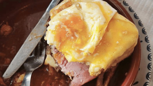 Dish with meat, cheese, and egg on top, a fork and knife on the side.