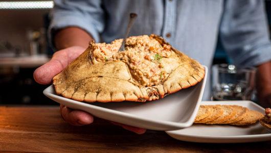 Hand holding a crab shell filled with seafood dish on a plate.
