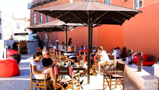 People dining outdoors at a cafe with umbrellas and red building backdrop.