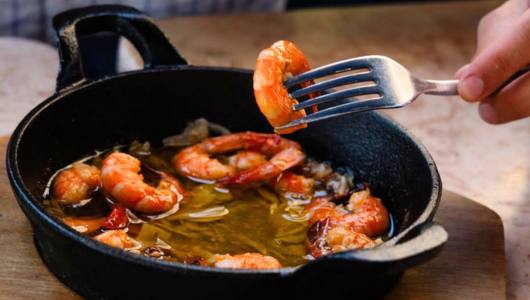 Fork holding shrimp over skillet with sizzling oil and more shrimp.