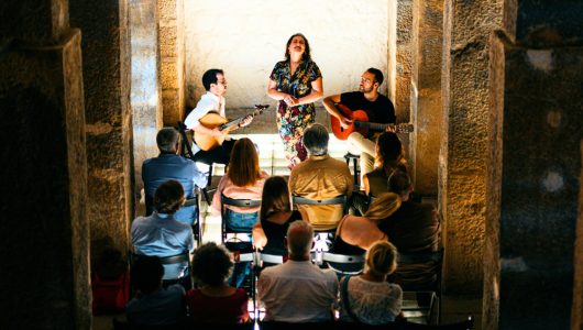 Trio performing music for seated audience in stone-walled room.