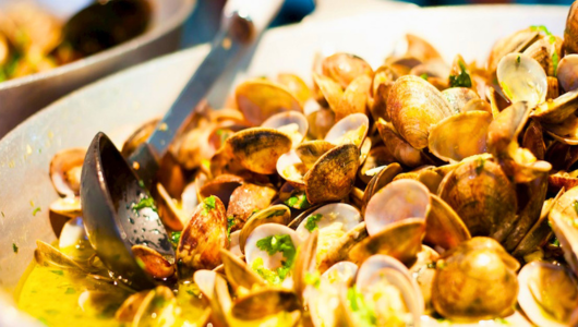 Close-up of cooked clams in a pan with herbs and sauce.